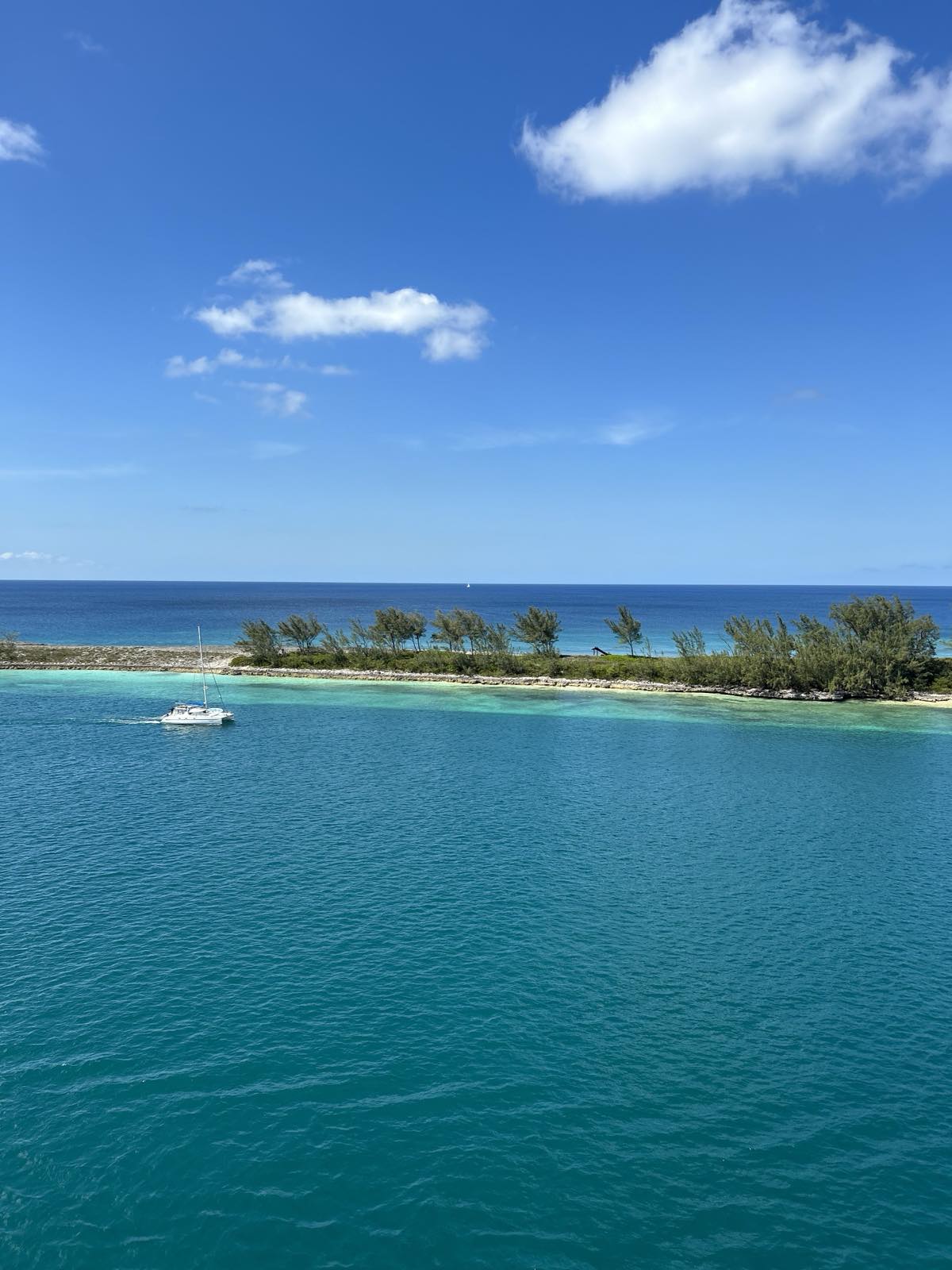 Turquoise water and a small island seen from a cruise ship, with a sailboat passing by